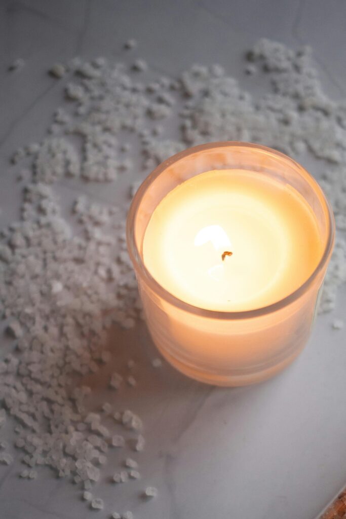 High angle of jars with colorful natural salt for bath placed near burning candle on white marble table